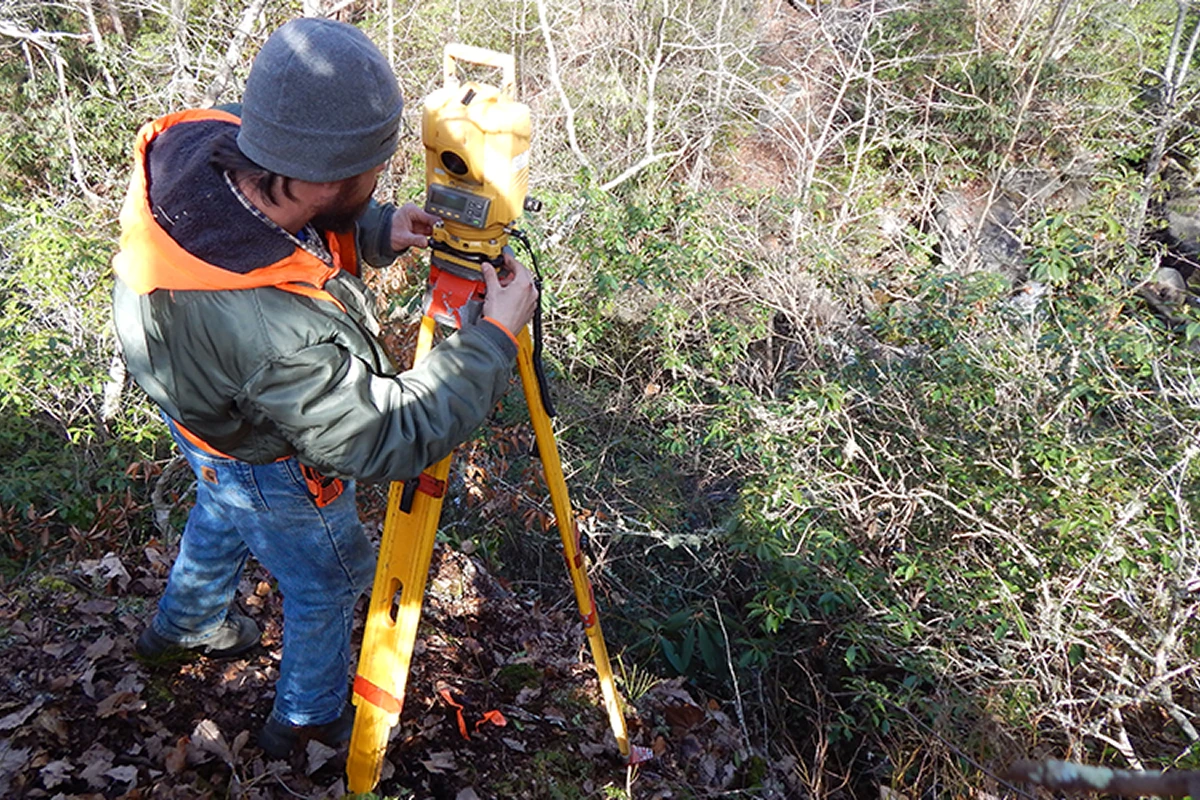 Surveyor using equipment in a wooded area.
