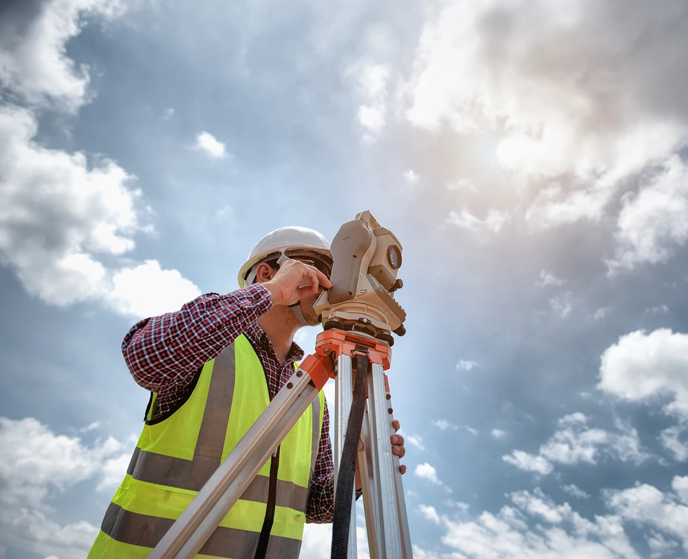 Surveyor using equipment under a cloudy sky.