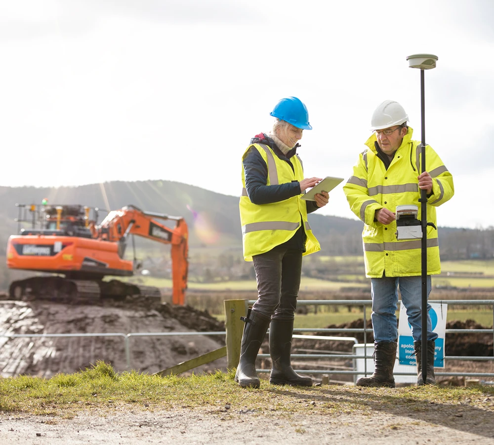 Construction workers using surveying equipment on site.