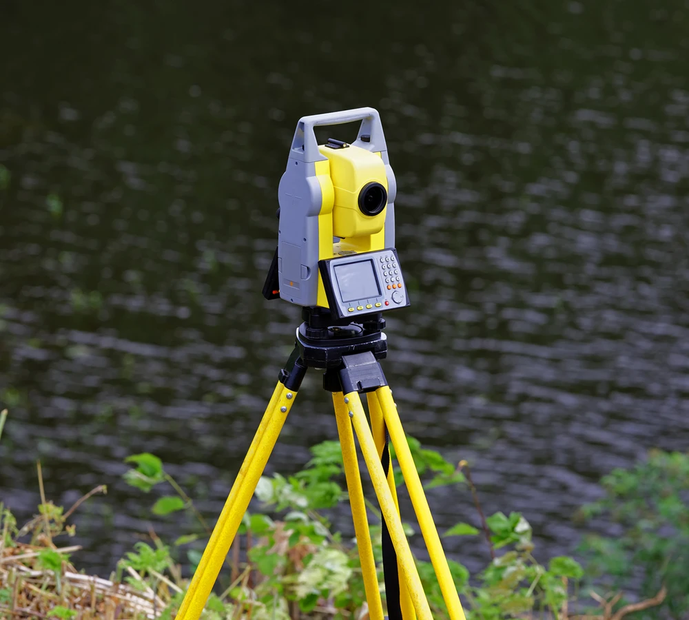 Surveying equipment on tripod near water.