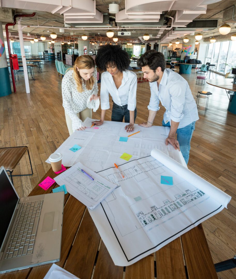People collaborating over architectural plans on table.