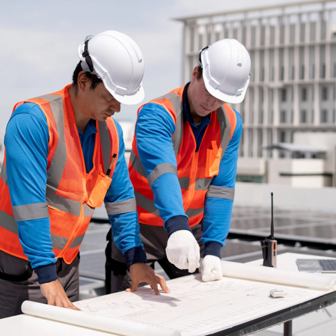 Workers reviewing blueprints on rooftop solar panels.